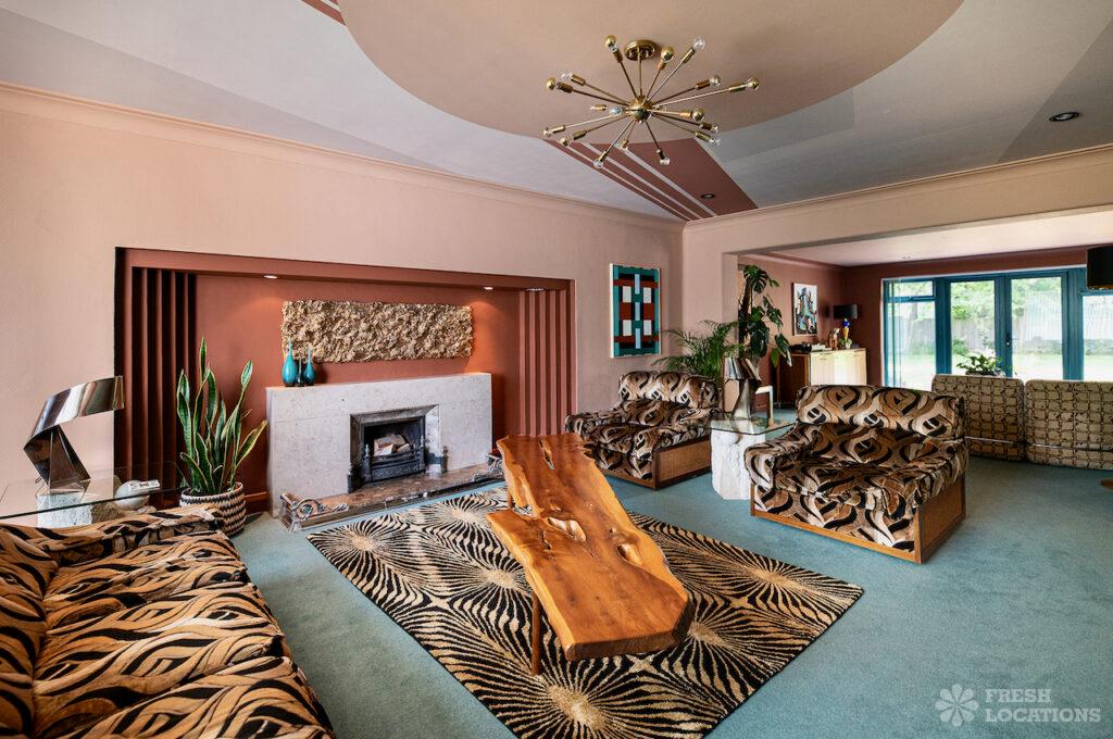 Retro shoot locations: step inside timeless homes for standout shoots 5 Eclectic retro-style living room at bardot bay shoot location in kent, featuring bold patterned sofas, a sculptural wooden coffee table, a graphic print black and brown rug, fireplace with textured wall art, and statement ceiling light fixture.