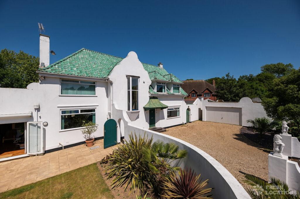 Retro shoot locations: step inside timeless homes for standout shoots 6 Exterior of bardot bay shoot location in kent, a striking white house with green tiled roof, curved architectural details, arched doors, and a gravel driveway framed by tropical plants and statues.